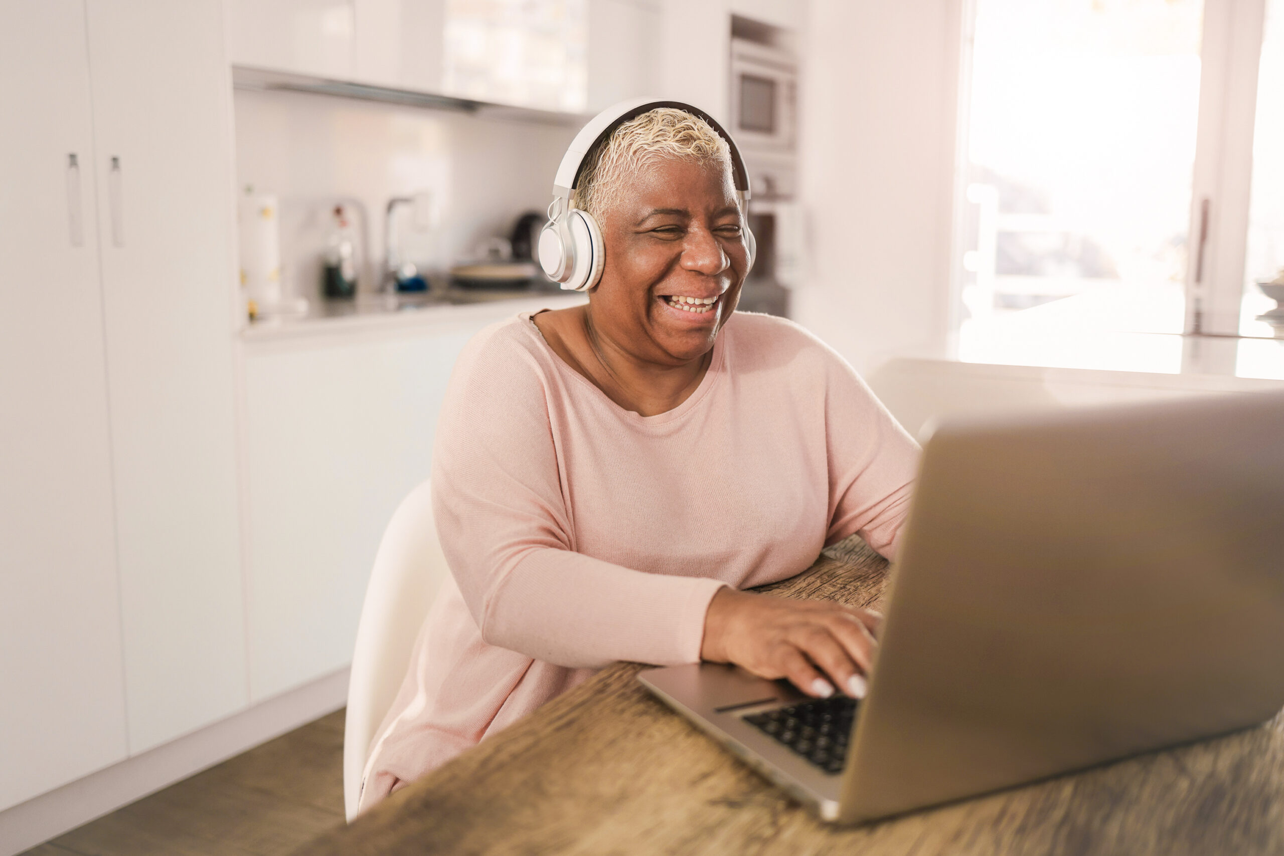 Senior,Woman,Using,Laptop,While,Wearing,Headphones,At,Home,- Senior woman using laptop while wearing headphones at home - Joyful elderly lifestyle and technology concept - Focus on face