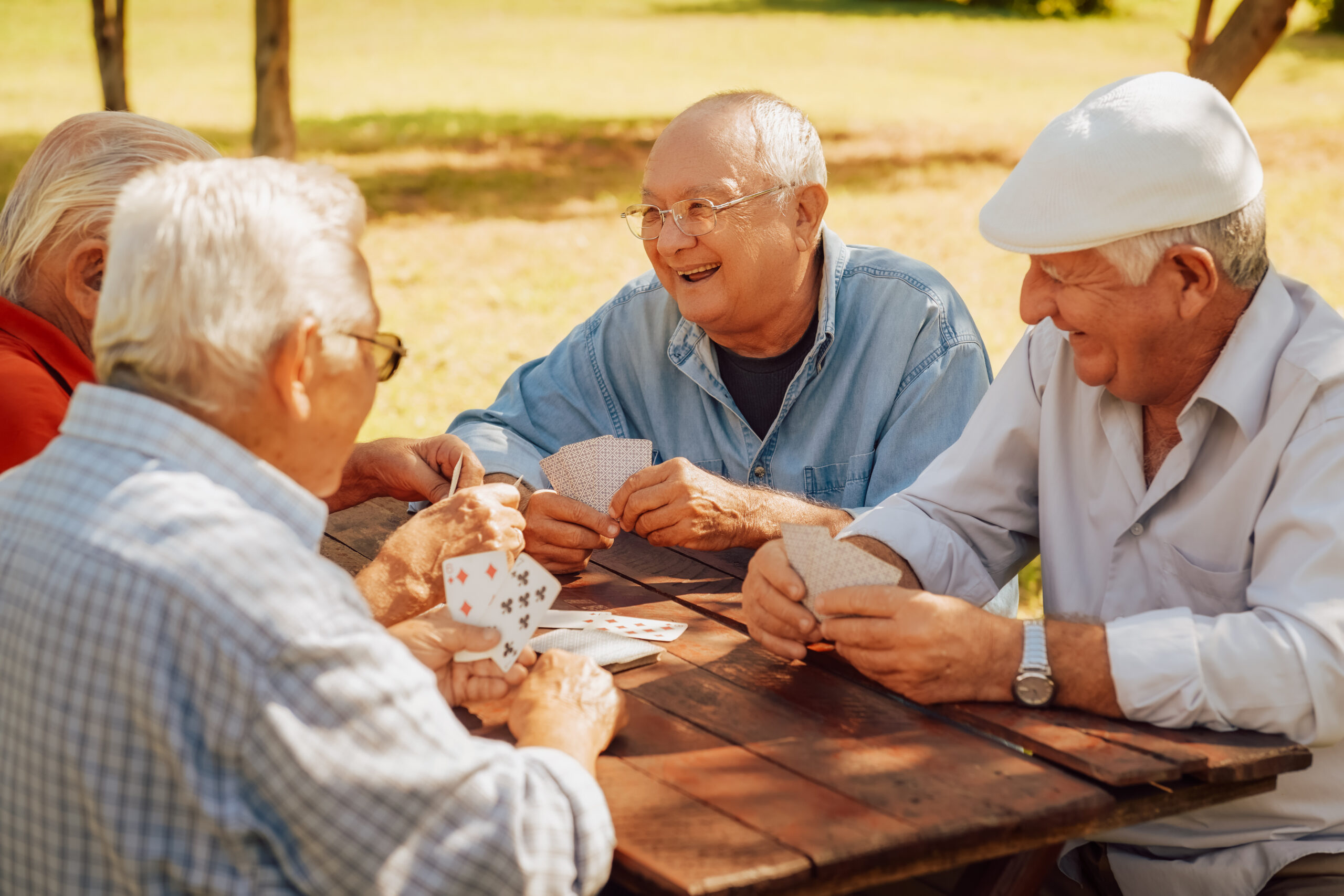 Active retirement, old people and seniors free time, group of four elderly men having fun and playing cards game at park. 