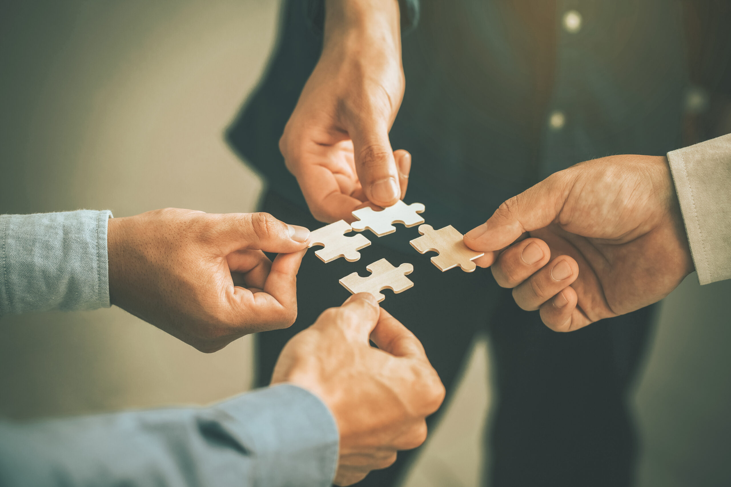Hands holding jigsaw pieces to form a single shape Hands holding jigsaw pieces to form a single shape