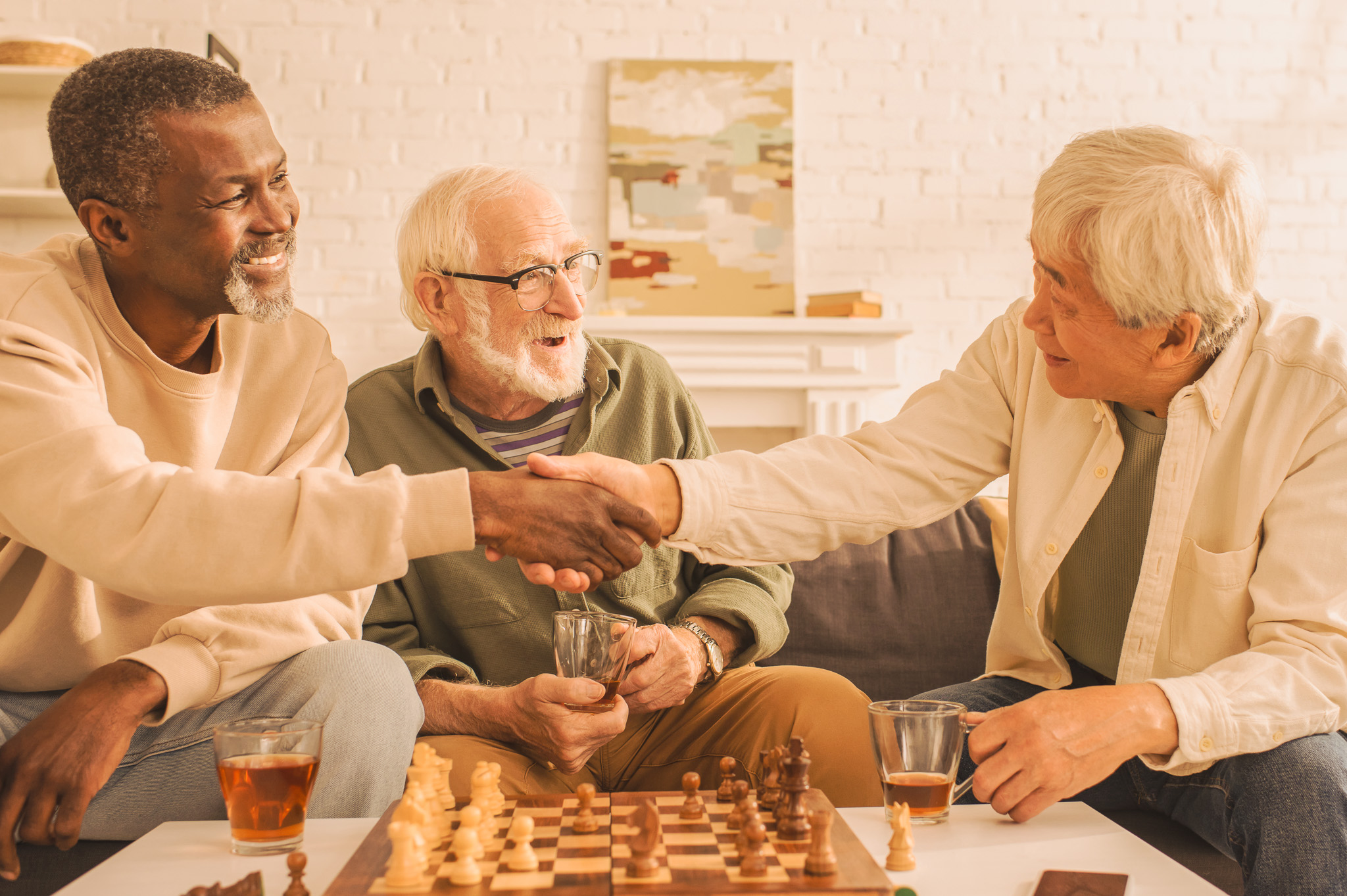 Multiethnic,Friends,Shaking,Hands,Near,Tea,And,Chess,At,Home Multiethnic friends shaking hands near tea and chess at home